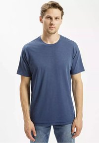 Granatowy, krótki rękaw T-shirt z miękkiego materiału, z okrągłym dekoltem i subtelnym logo na klatce piersiowej. Noszony z jasnymi dżinsami.