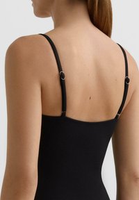 Črni rebrasti top z okroglim izrezom in tankimi nastavljivimi naramnicami s srebrnimi okraski. Gladek tekstura z oprijetim krojem.
