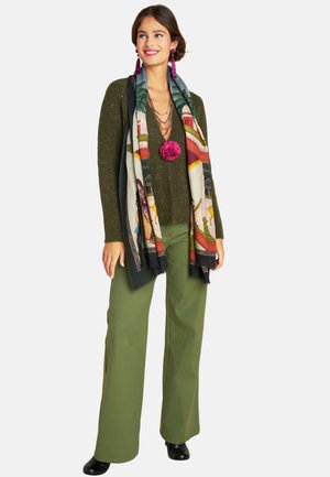 Green metallic knit sweater, wide olive green pants, patterned scarf with vibrant colors, black ankle boots, layered necklaces, and floral accent.