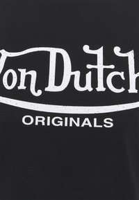 Černé bavlněné tričko s logem "Von Dutch" v opotřebovaném bílém písmu a se slovem "ORIGINALS" pod ním tučně. Hladká textura.