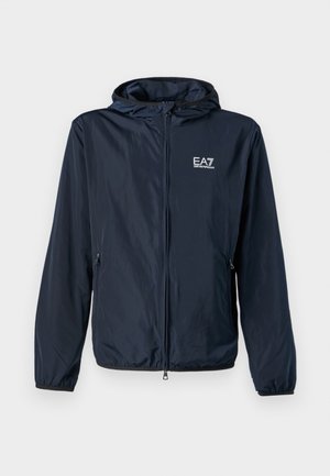 Námornícky vetrovka s predným zipsom, nastaviteľnou kapucňou, bočnými zipsovými vreckami a logom na ľavej hrudi. Hladká textúra, ľahký materiál.