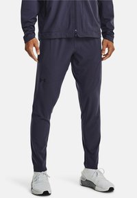 Pantalones deportivos navy con un corte ajustado, hechos de tejido que absorbe la humedad, con bolsillos laterales con cremallera y detalle del logo en el muslo izquierdo.