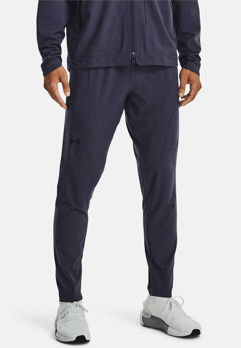 Pantalones deportivos navy con un corte ajustado, hechos de tejido que absorbe la humedad, con bolsillos laterales con cremallera y detalle del logo en el muslo izquierdo.
