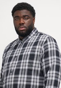 Black and white plaid shirt with a button-down collar, featuring a chest pocket and a smooth cotton texture.