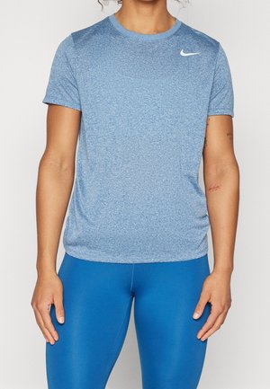 Persoon die een lichtblauw Nike sportshirt met korte mouwen en felblauwe legging draagt, staand tegen een effen achtergrond.