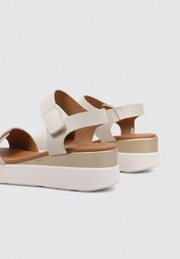 Sandalias de plataforma beige con correas de cuero texturizado y cierres ajustables. Plantilla acolchada, acentos en dorado contrastante y suela blanca.
