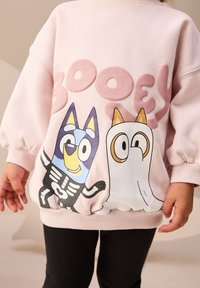 Sweat-shirt rose clair avec des personnages de dessin animé et le texte "BOO". Comprend des poignets et un ourlet côtelés, un tissu doux, et une impression graphique audacieuse.