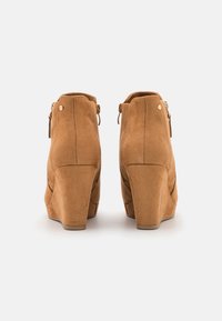 Botas de tornozelo em camurça castanha com fecho de zíper na parte de trás, apresentando uma textura suave e um design de salto estruturado em cunha.