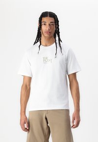 Tricou alb din bumbac cu mâneci scurte și guler rotund, având un imprimeu aurie care scrie "PLANTA" pe față.
