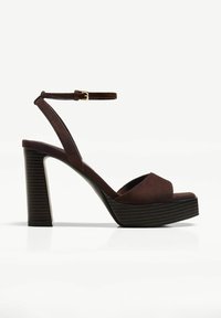 Sandali con tacco alto in suede marrone, dotati di cinturino alla caviglia regolabile e suola piattaforma chunky con una texture rigata verticale.