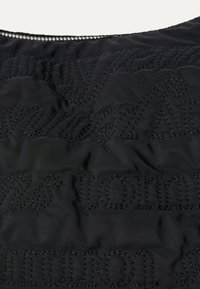 Tissu matelassé noir avec un texte en relief dans une finition mate contrastante. Texture simple et douce avec des détails de couture minimalistes.