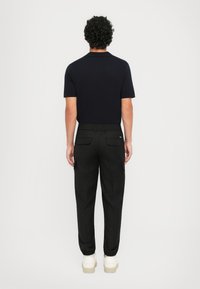 Marineblå polo T-shirt parret med sorte cargo bukser med elastisk talje, sidelommer og elastiske manchetter; båret med hvide sneakers.
