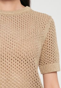 Top corto a maniche corte in maglia dorata con un design aperto e simile a rete, dotato di una scollatura e polsini a coste, che conferisce un aspetto leggero e testurizzato.