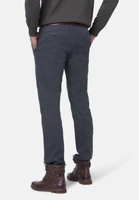 Grå smala byxor i mjukt material. Har två bakfickor, bälteslipsar och en avsmalnad design. Bärs med bruna snörkängor.