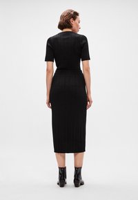 Rochie tricotată neagră cu dungi, cu mâneci scurte, talie strânsă și lungime midi. Purtați cu botine negre până la gleznă cu toc pătrat.