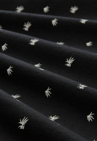 Tela negra con un patrón repetido de pequeñas hojas de palma blancas; textura suave con un ligero brillo, cayendo en suaves pliegues.