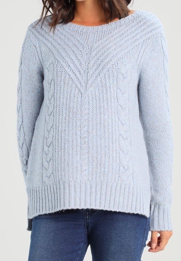 Pull bleu clair en maille torsadée avec manches longues et ourlet côtelé, porté avec un jean bleu foncé.