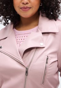 Rosa Kunstleder-Motorradjacke mit silbernen Reißverschlüssen, Druckknopf und einem strukturierten hellrosa Oberteil darunter mit rundem Ausschnitt.