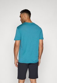 Turkise t-skjorte med korte ermer laget av lett stoff, kombinert med svarte shorts; har rund hals og avslappet passform.