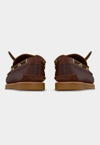 Καφέ δερμάτινα παπούτσια τύπου boat με ταμπά λαστιχένιες σόλες, ραμμένες λεπτομέρειες και διπλωμένες γλώσσες, εμφανιζόμενα από πίσω σε λευκό φόντο.