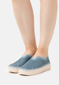 Zapatillas azul de tipo slip-on con parte superior de malla estampada, suela texturizada beige y diseño de punta redondeada. Material ligero y transpirable.