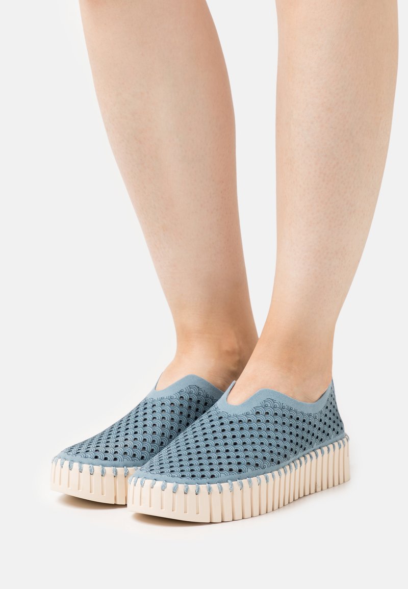 Zapatillas azul de tipo slip-on con parte superior de malla estampada, suela texturizada beige y diseño de punta redondeada. Material ligero y transpirable.