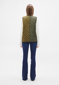 Γιλέκο καπιτονέ με σχεδιασμό σε μπλοκ χρωμάτων με πράσινες και ελαιώδεις πίνακες. Κατασκευασμένο από υφή υφάσματος, έχει ευθεία κοπή και δεν διαθέτει κουκούλα.