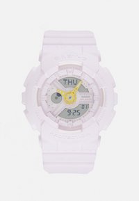 Reloj digital de color púrpura claro con una caja redonda resistente a los golpes, pantalla analógico-digital, acentos amarillos y correa de goma. Las características incluyen indicadores de hora y día.