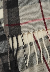 Écharpe en laine présentant un motif à carreaux en noir, gris, blanc et rouge, avec des bords frangés pour plus de texture.