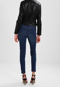 Giacca da biker in pelle nera, jeans skinny blu scuro aderenti e sandali neri con tacco alto. Tessuto liscio con due tasche posteriori visibili.