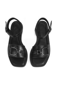 Black leather sandals with an adjustable ankle strap, square toe shape, large decorative buckle on the front, and a smooth texture.