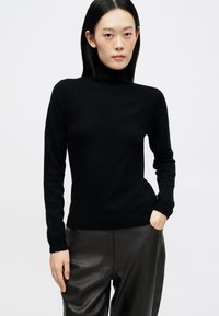 Pulôver preto de gola alta em um design ajustado, com mangas longas, feito de um material suave. A textura parece lisa e aconchegante.