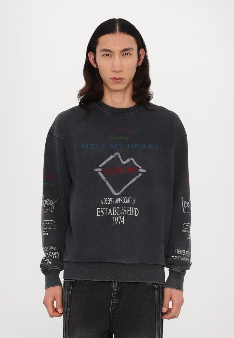 Sweatshirt gris foncé à col rond, arborant un texte et des logos multicolores, des poignets côtelés et une coupe oversize.