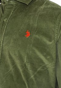 Camicia di velluto a coste verde con bottoni e un piccolo logo ricamato rosso di un giocatore di polo a cavallo sul petto.