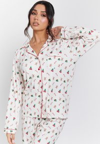Witte pyjama set met afbeeldingen van peperkoekmannetjes, kerstbomen en zuurstokken. Rode biesaccenten, knoopsluiting met zakje en lange mouwen.