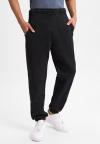  Sorte joggerbukser med elastisk talje, sidelommer og tætsiddende cuffs. Fremstillet af blødt stof, med en glat tekstur og simpelt design.