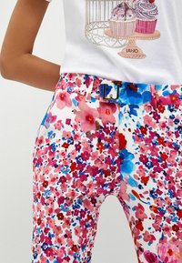 Witte broek met levendig roze, rode en blauwe bloemenpatroon, gecombineerd met een bijpassende bloemenriem met een metalen "LJ" gesp.