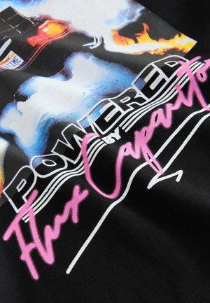 Camiseta negra con un estampado gráfico que muestra un coche llameante y el texto "ALIMENTADO por el Condensador de Fluzo" en cursiva blanca y rosa sobre la tela.