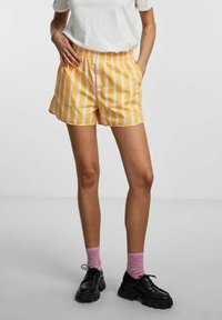 Gule og hvide stribede shorts med elastisk talje, sidelommer. Kombineret med sorte platformssko og lyserøde sokker.