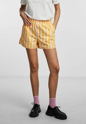 Gule og hvide stribede shorts med elastisk talje, sidelommer. Kombineret med sorte platformssko og lyserøde sokker.