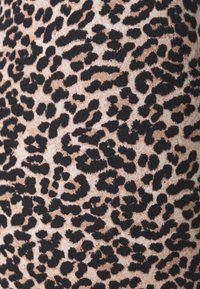 Tyget med leopardmönster har en beigefärgad bakgrund med oregelbundna svarta fläckar, vilket ger en strukturerad look. Mönstret är djärvt och framträdande.