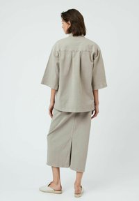 Chemise en coton gris clair à coupe décontractée et manches courtes, assortie d'une jupe mi-longue avec une fente arrière.
