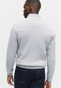 Jasnoszary sweter w warkocze z wysokim kołnierzem, ściągaczem u dołu i na mankietach. Wyróżniający się fakturowany wzór na plecach i rękawach.
