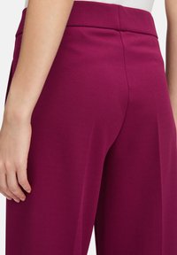 Strakke, hoge taille broek in een rijke bordeauxkleur. Gemaakt van een gladde, zachte stof met een op maat gemaakte snit die de strakke lijnen benadrukt.