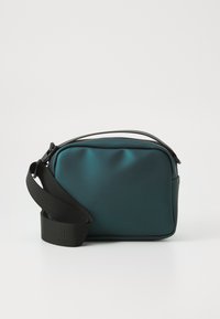 Borsa a tracolla impermeabile di colore teal con texture liscia, tracolla nera regolabile e branding discreto sul davanti. Forma rettangolare.