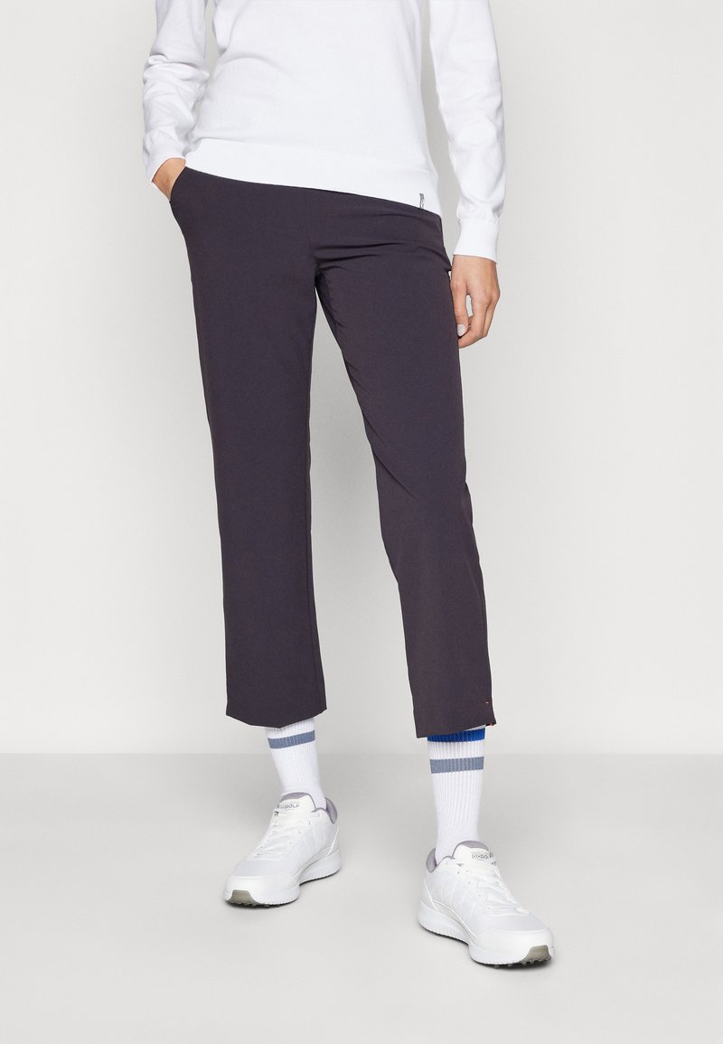 Calças slim-fit de cor roxa escura, com uma textura suave e comprimento curto, combinadas com sapatilhas brancas e meias de cano curto às riscas.