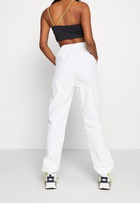 Joggers blancs légers à coupe décontractée, avec une bande latérale jaune néon, associés à un haut court noir et des chaussures sportives.