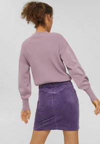 Fliederfarbener, gerippter Pullover mit langen Ärmeln, kombiniert mit einem Minirock aus lila Cord mit zwei Gesäßtaschen und einem flachen Bund.