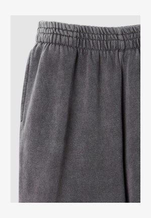 I pantaloni grigi in felpa hanno una texture morbida, una cintura elastica e tasche laterali. Il tessuto presenta un motivo a maglia uniforme.
