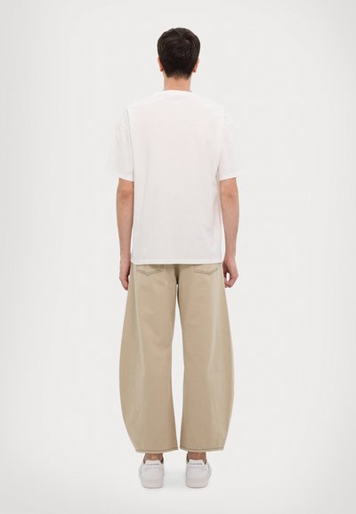 Camiseta de algodón blanca de manga corta, combinada con pantalones de pierna ancha beige. Los pantalones cuentan con dos bolsillos traseros y un ajuste relajado.